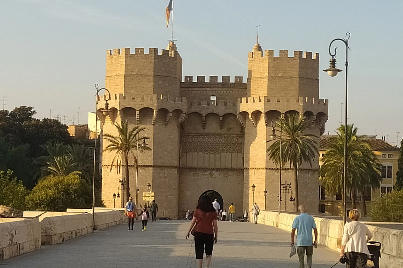 The Torres de Serranos, a crenellated stone city gate in warm evening light, seen from its bridge approach